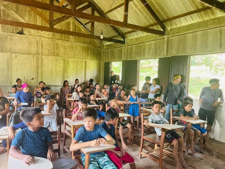 Crianças indígenas em sala de aula. A sala abriga vários jovens e a estrutura do local é simples